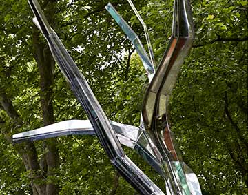 a tree structure made of shiny metal in front of branches of real trees with green leaves
